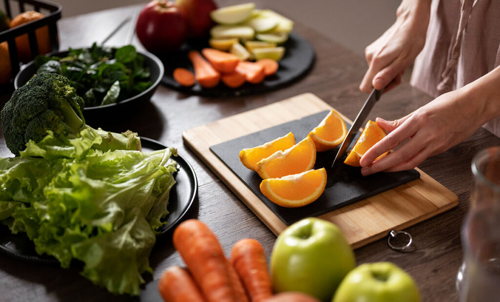 Woman cutting an orange with other fruits and vegetables.