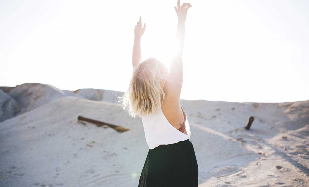 A young woman raising her arms toward the sun.