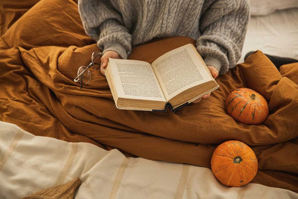 Woman reading in bed near pumpkins.