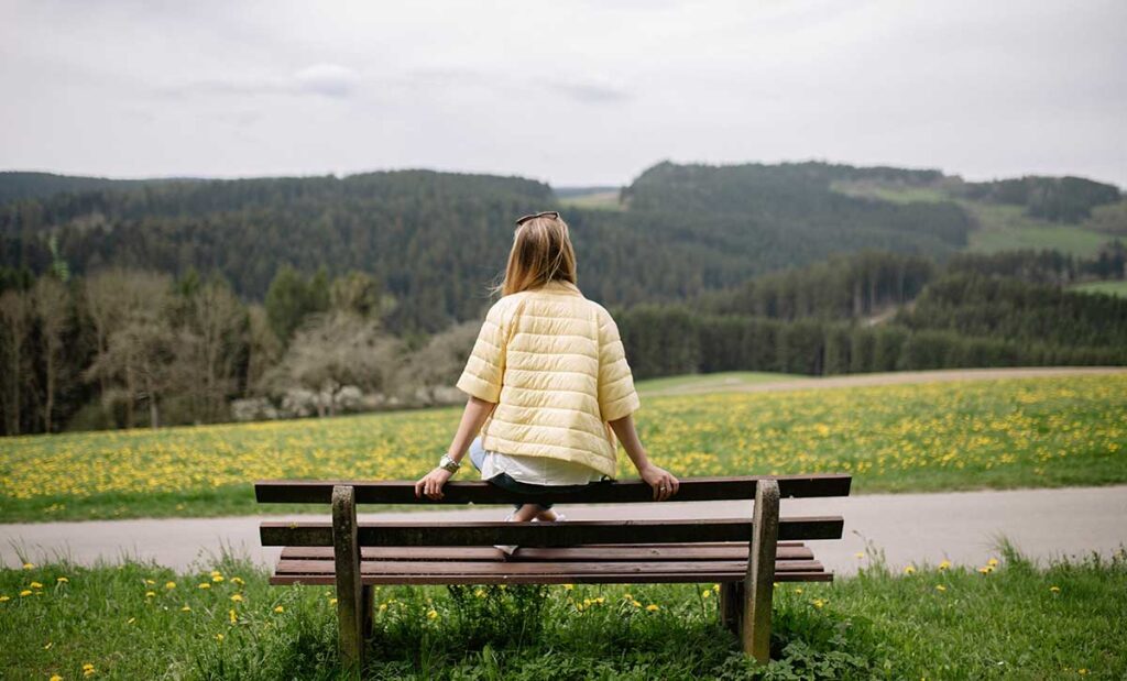 Woman sitting on a bench looking at mountains.