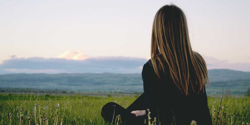 Young woman sitting outside on a field of grass.