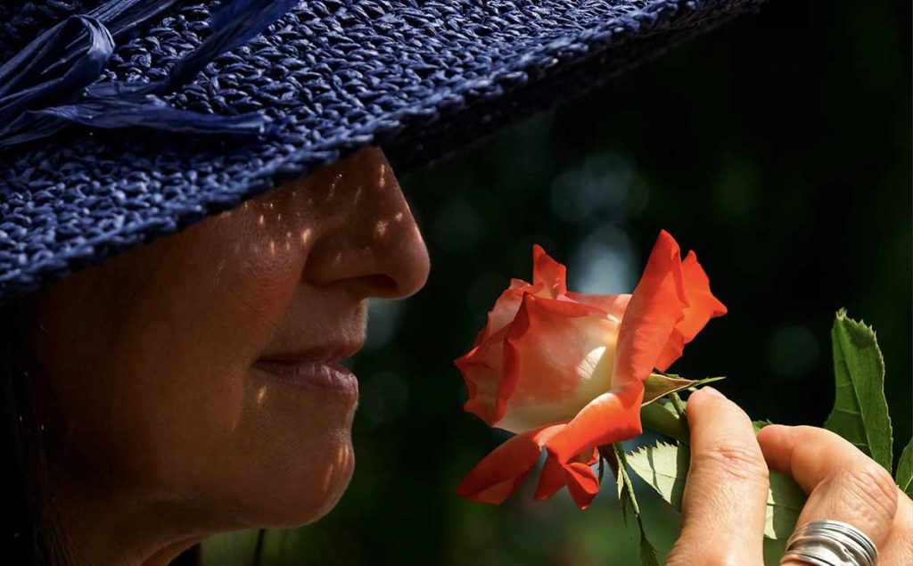 Woman in big blue hat smelling a rose