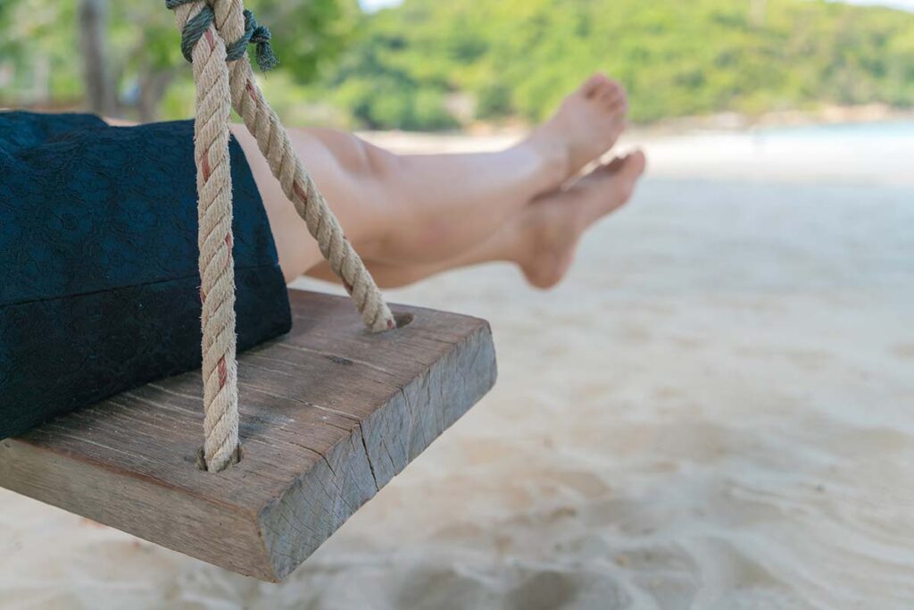 Close up of woman on a wooden swing on a beach.