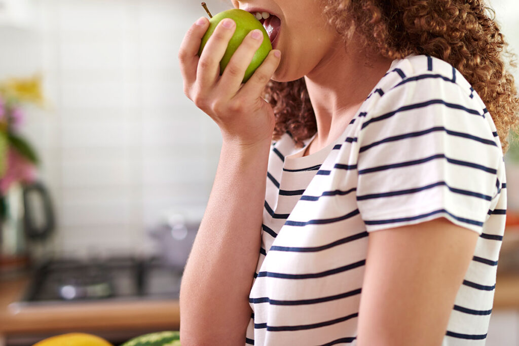 Red headed woman in striped shirt taking a bite out of a green apple.