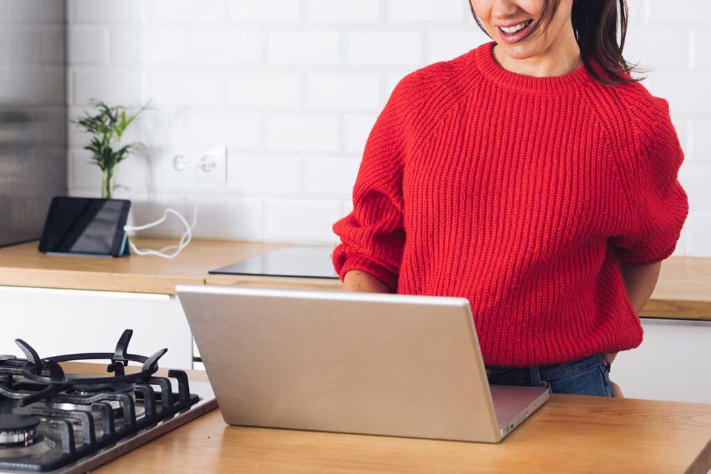 Woman in red sweater using laptop in kitchen.