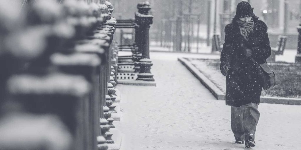 Woman walking on sidewalk during a snow blizzard.