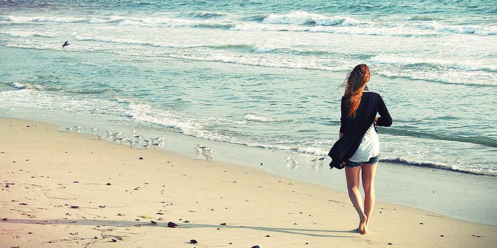 Young woman in shorts walking on beach barefoot.