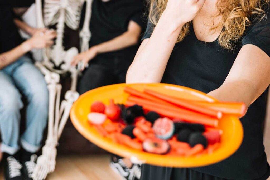 Young woman at Halloween party holding out a plate of healthy food.