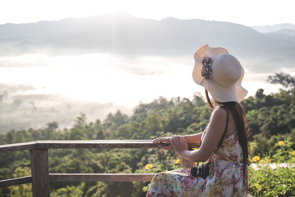 Woman with big floppy hat and a camera looking at a mountain view.