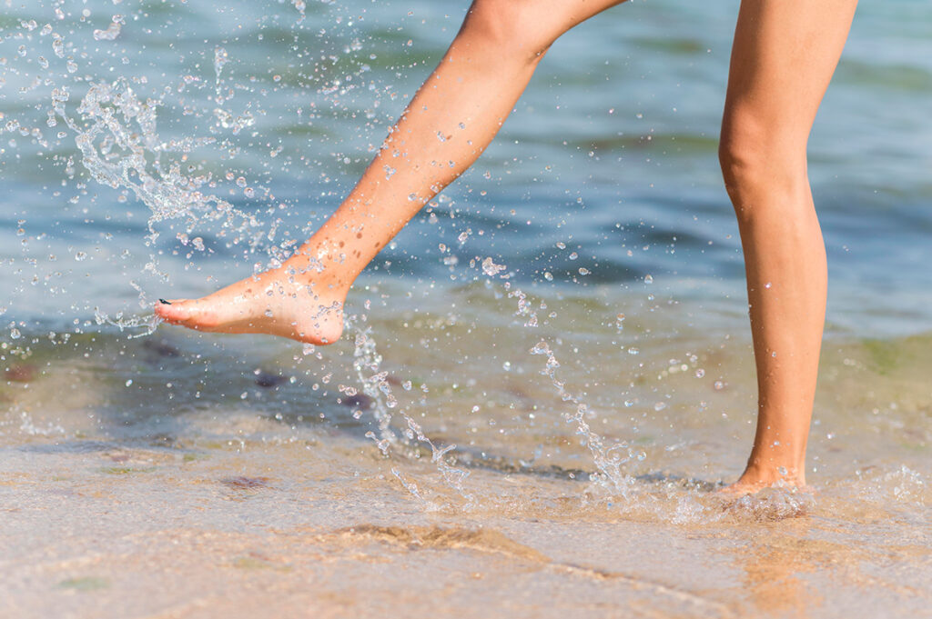 Closeup of woman's feet splashing in the water on the beach.