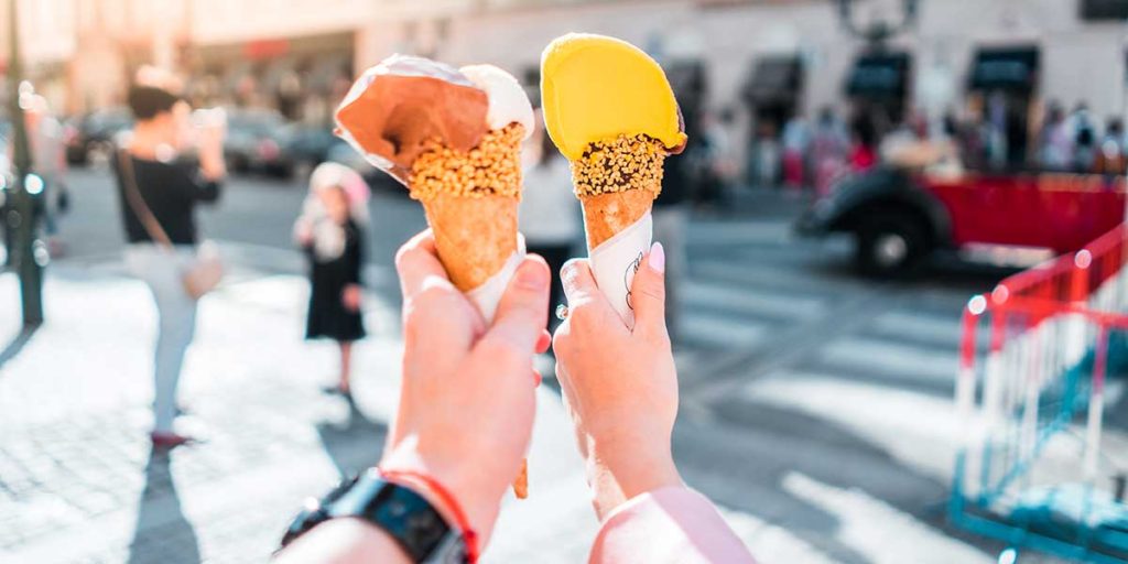 A young couple holding out ice cream cones.