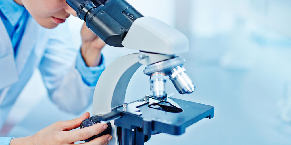 Young female chemist looking in microscope.