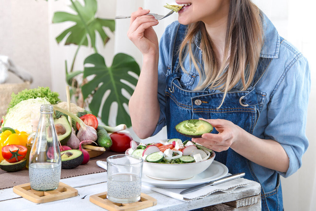 Young and happy woman eating salad at the table.