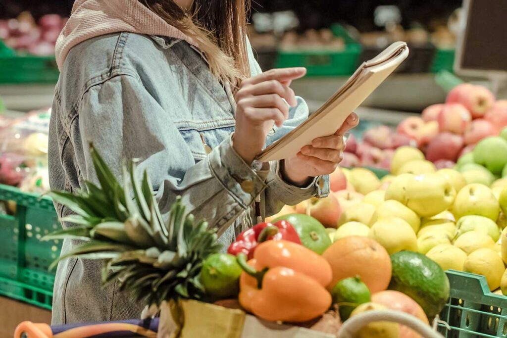 Young woman holding a notebook shopping for produce.