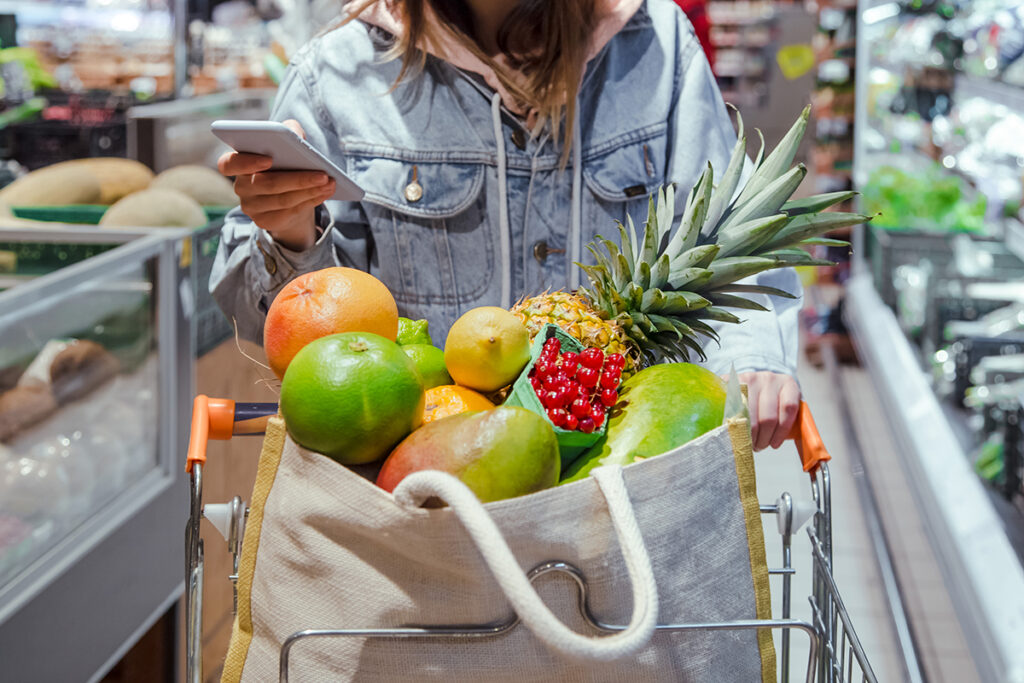 Young woman with grocery bag full of fruit looking at her smartphone.