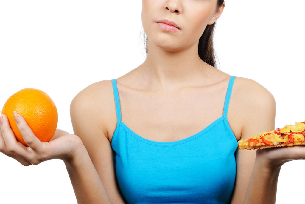 Young woman choosing between a pizza or an orange.