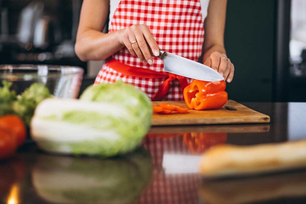 Young woman in a red and white checkered apron chopping.a red bell pepper.