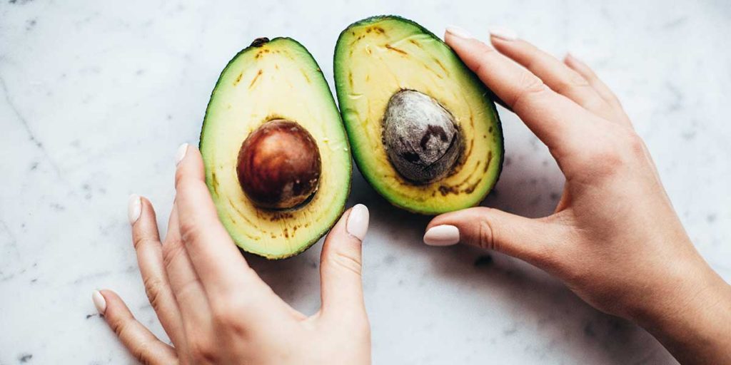 Young woman holding avocado halves on table.