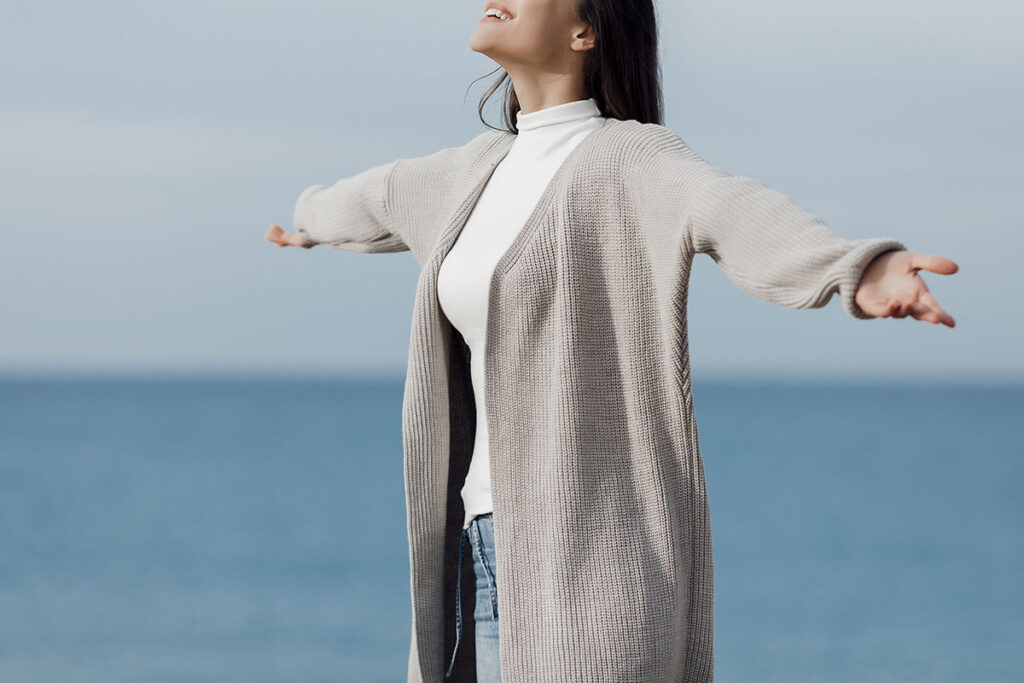 Young woman outdoors near water stretching arms to side.