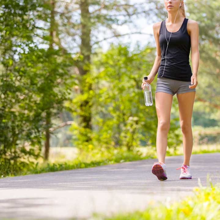 Young woman walking on path with water bottle and earbuds.