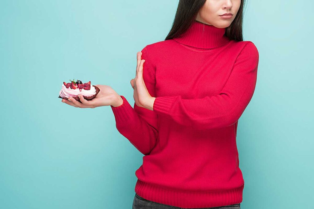 Young women in red sweater holding small cake with blue background.