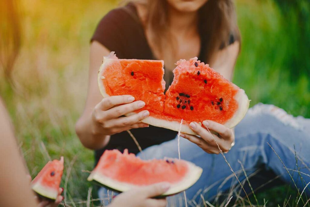 Young women sitting on the grass eating watermelon.