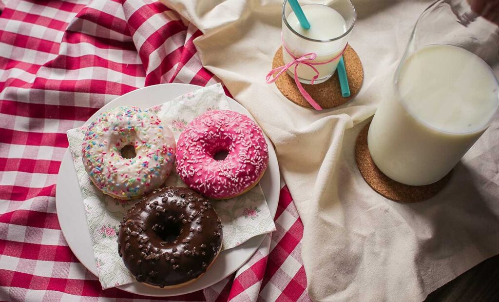 A bottle of milk with glass of milk and three donuts on a plate.