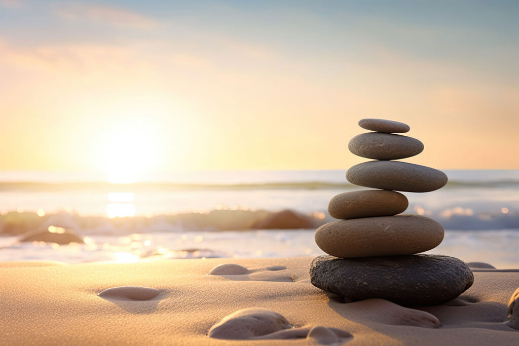 Zen stones balanced on a beach with a sunrise shining on the ocean.